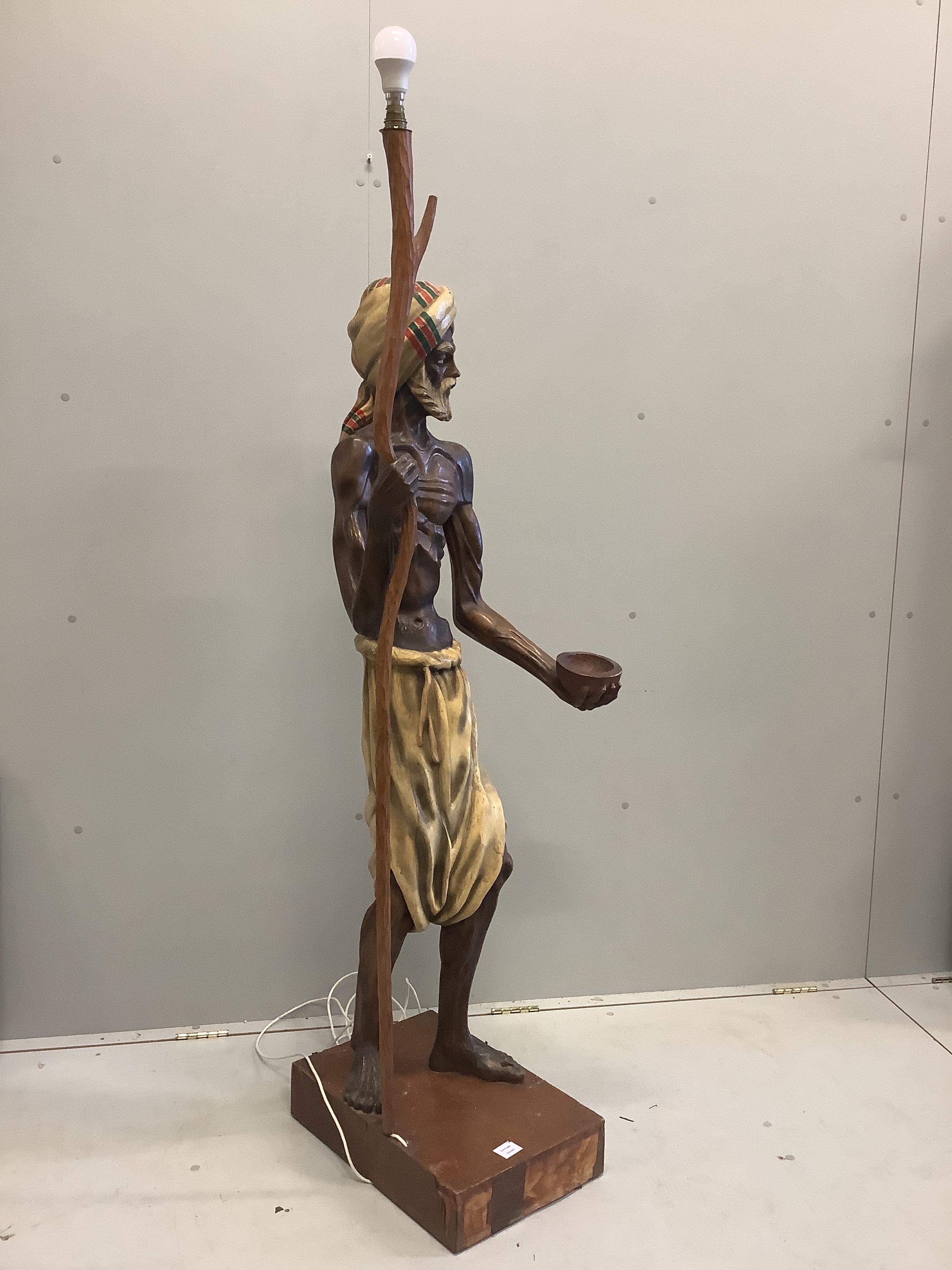 A carved wood lamp standard modelled as a beggar with a bowl and a staff, height 168cm